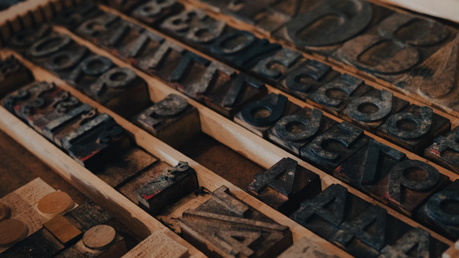 Worn wooden letterpress type sorted into the rows of a type case, each piece kept in its own compartment and set into one page together, the way roles stay distinct while the work moves between them