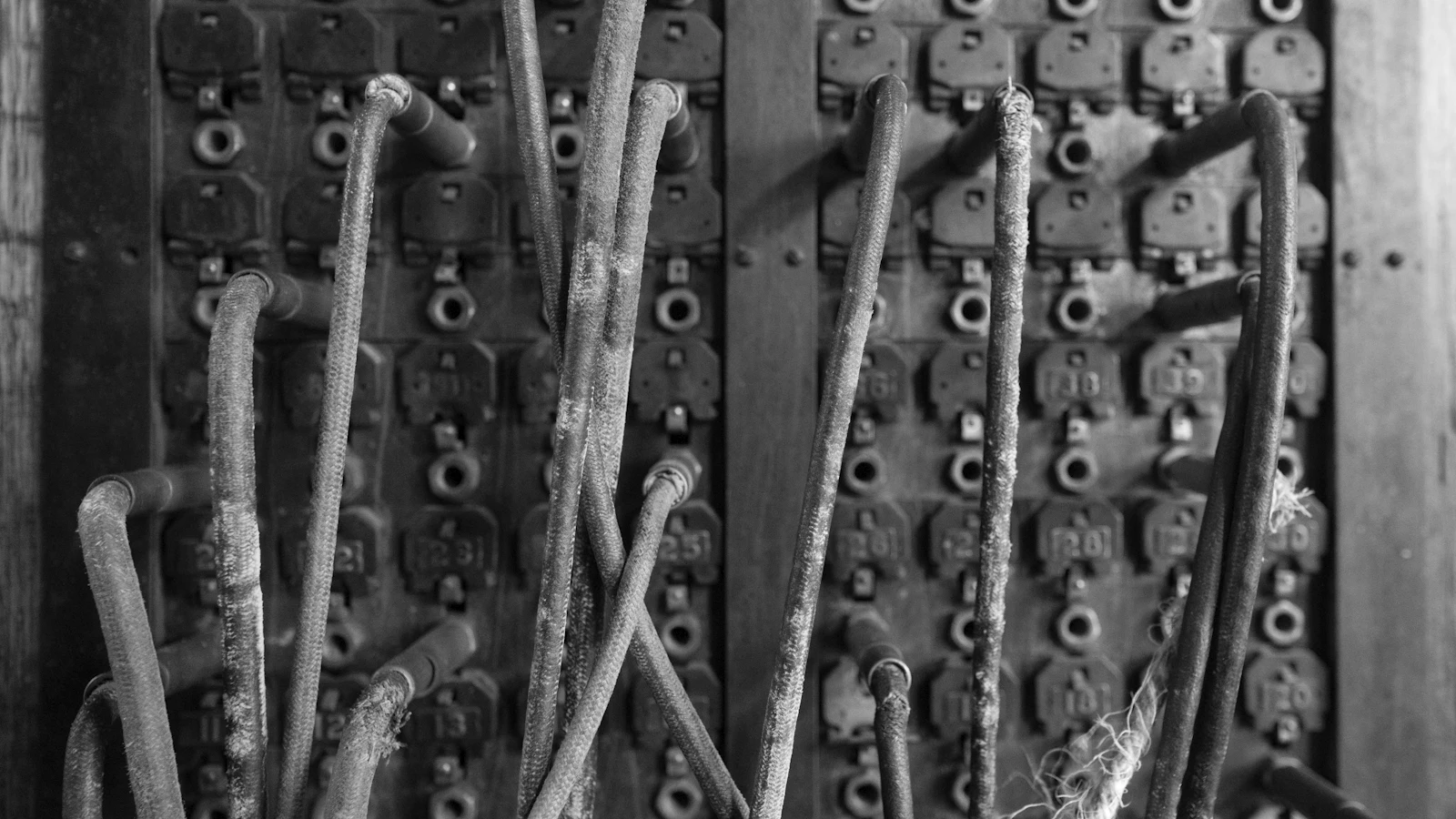 A disused manual telephone switchboard, its numbered jacks and frayed patch cords still plugged in — every call once passed through one board, where whoever worked it heard all of them